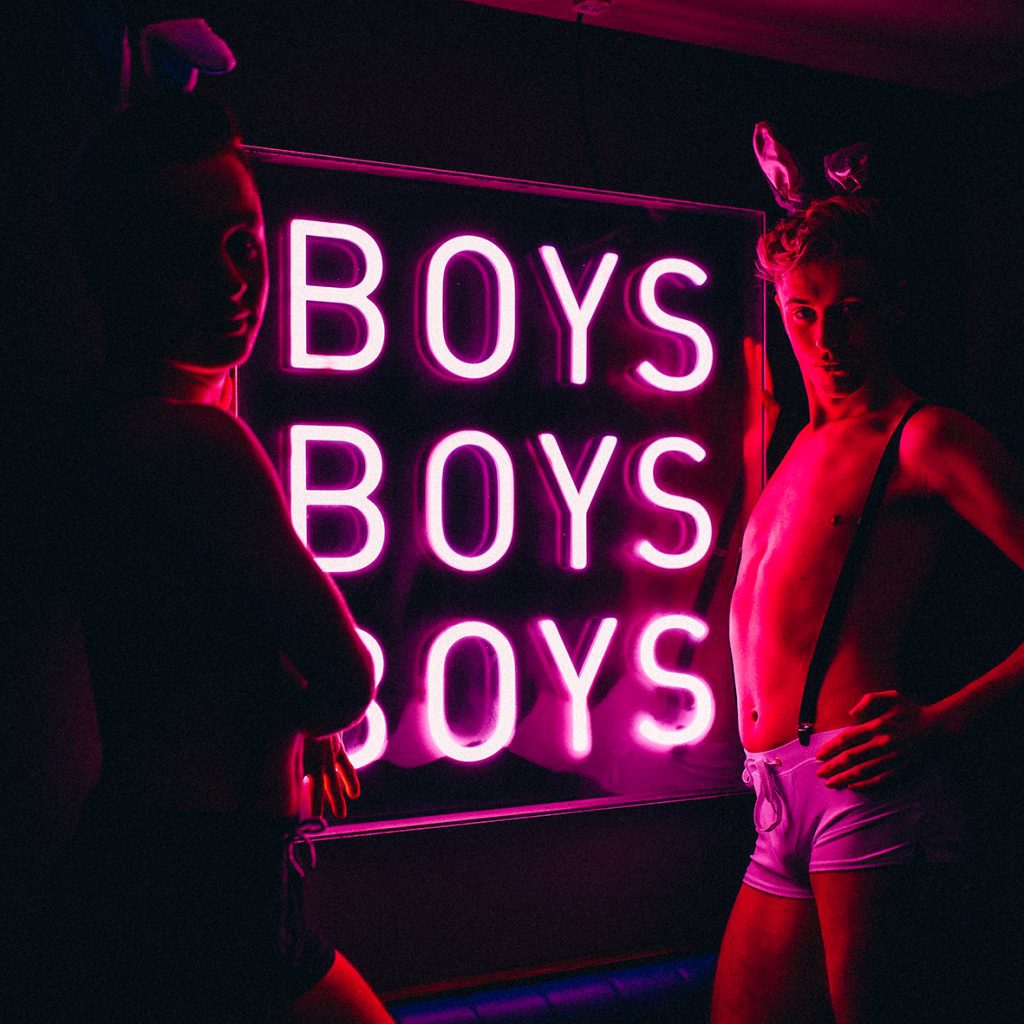 Two men standing in front of a neon sign wearing bunny outfits